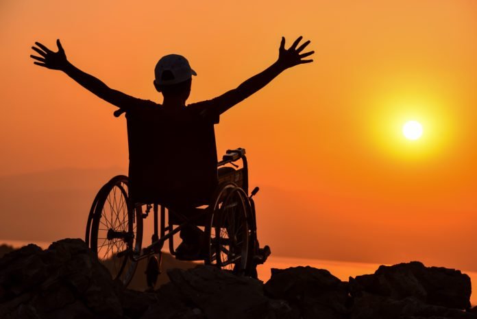 Descrição da imagem #PraCegoVer: A imagem está no formato retangular, na horizontal. Nela, uma pessoa está sentada em sua cadeira de rodas. É possível ver apenas a sombra da pessoa, que está com os braços abertos. Fim da descrição.
