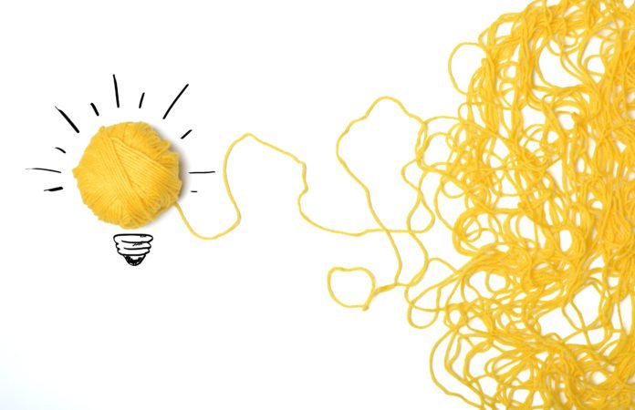 Descrição da imagem #PraCegoVer: Imagem no formato retangular, na horizontal. A imagem tem fundo branco. Do lado direito temos um novelo de lã amarela solto, que se transforma em uma lâmpada. Ao redor do novelo, que forma a lâmpada, temos o desenho de um bocal e traços circundando o novelo, remetendo à chama da lâmpada. Fim da descrição.
