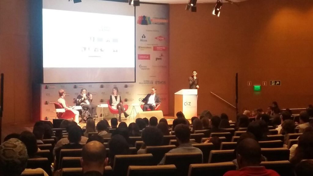 Descrição da imagem #PraCegoVer: Imagem no formato retangular, na horizontal. Nela vemos o palco do fórum da diversidade. No palco estão quatro pessoas, sendo uma delas, um intérprete de Libras. Fim da descrição.