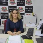 Descrição da imagem #PraCegoVer: Imagem no formato retangular, na horizontal. Nela está a delegada Samanta Rihbani Conti, titular da Delegacia de Polícia da Pessoa com Deficiência. Ela é uma mulher branca, com cabelos loiros, cacheados e está sentada em sua mesa, na delegacia. Fim da descrição.