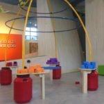 Descrição da imagem #PraCegoVer: Imagem no formato retangular, na horizontal. Uma das salas de recreação do Museu da Imaginação. Nela vemos uma estação do brincar em que as crianças precisam equilibrar uma mesa utilizando pequenos pesos. Fim da descrição.