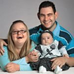 Descrição da imagem #PraCegoVer: Imagem no formato retangular, na horizontal. Nela estão Gabriela, que tem síndrome de Down, Fábio, que tem deficiência intelectual, e a pequena Valentina, filha do casal, que não tem deficiência. Eles estão sorrindo. Fim da descrição.