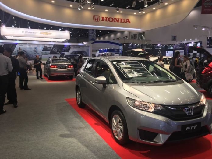 Descrição da imagem #PraCegoVer: O estande de uma montadora de carros com alguns modelos expostos durante a Reatech. Em destaque, um modelo Honda Fit, na cor cinza. Fim da descrição.