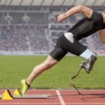 Descrição da imagem #PraCegoVer: A imagem está no formato retangular, na horizontal. Ela tem em destaque um paratleta de atletismo em um estádio. Ele está de lado, em posição de largada. O atleta usa uma prótese especial para corrida na perna direita. Ao fundo é possível ver a arquibancada do estádio cheia de pessoas. Fim da descrição.
