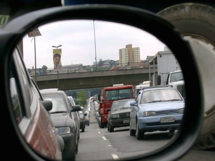 Descrição da imagem #PraCegoVer: A imagem está no formato quadrado. Nela é possível ver, a partir de um retrovisor do carro, duas fileiras de carros formando trânsito em uma rodovia. Fim da descrição.