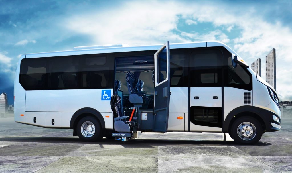Descrição da imagem #PraCegoVer: A imagem está no formato retangular, na horizontal. Nela está o micro-ônibus adaptado da IVECO, A imagem mostra a lateral do ônibus e é possível ver que ele está com a porta aberta. Com isso, podemos ver também o elevador de transferência dos passageiros com deficiência física para o interior do micro-ônibus. Fim da descrição.
