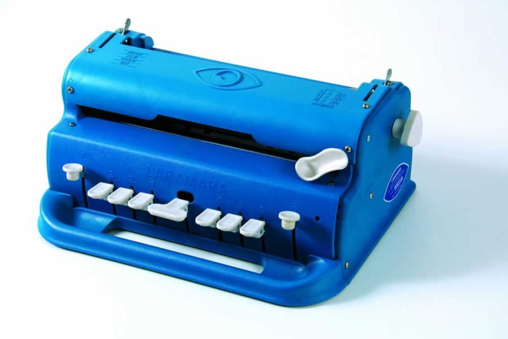 Descrição da imagem #PraCegoVer: A Imagem está no formato retangular, na horizontal. Nela, é possível ver a máquina de escrever em braile. Ela é azul e tem as teclas na cor cinza. Fim da descrição