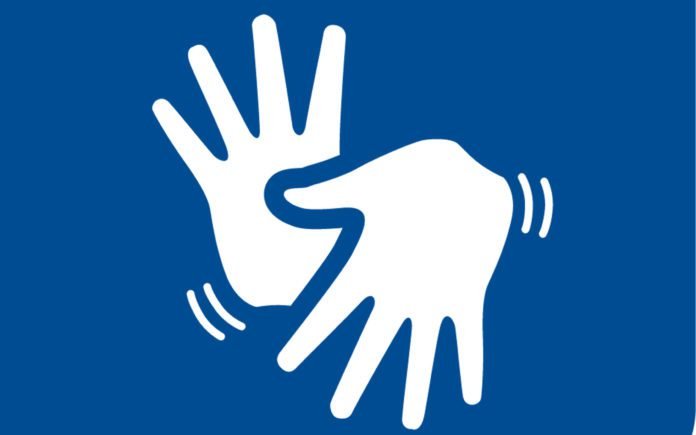 Descrição da imagem #pracegover: Ilustração do símbolo da Língua Brasileira de Sinais (Libras). Nele estão duas mãos, sobrepostas. Elas são brancas. A imagem tem um fundo azul. Fim da descrição.