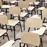 Descrição da imagem #PraCegoVer: Imagem no formato retangular, na horizontal. A Imagem é de uma sala de aula, com diversas carteiras na cor bege, vazias enfileiradas. Entre elas estão cadeiras com braços para destros e canhotos. Fim da descrição.