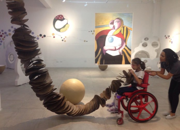 Descrição da imagem #PraCegoVer: Imagem no formato retangular, na horizontal. Sofia está brincando e interagindo com objetos expostos no museu, em uma atividade sensorial proposta pela monitora do espaço. Fim da descrição.
