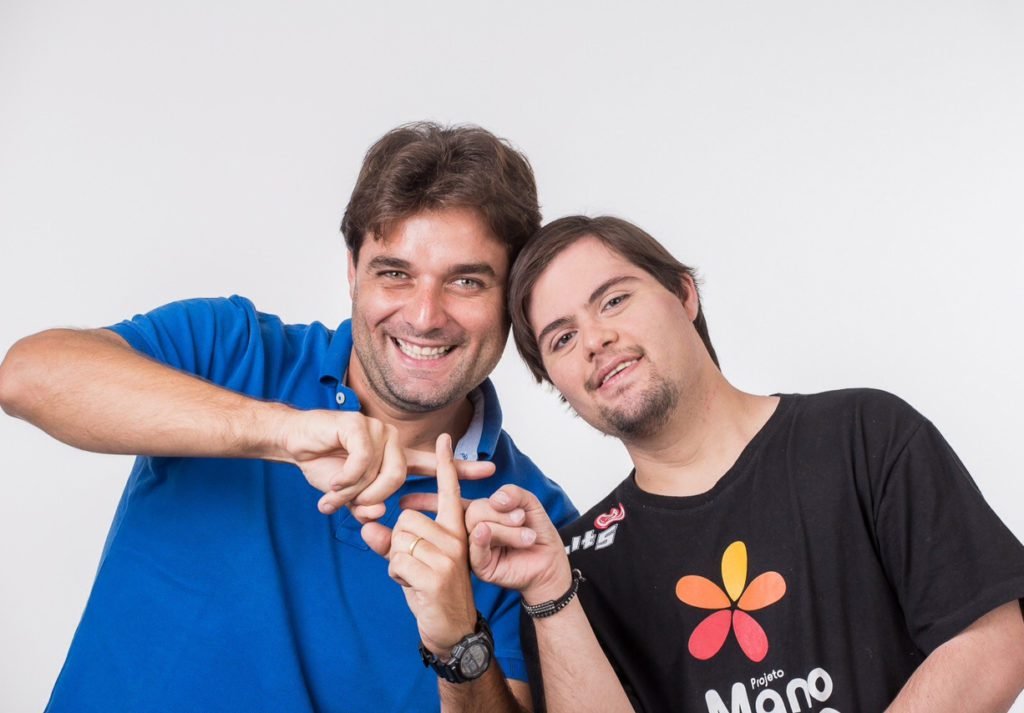 Descrição da imagem #pracegover: O colunista Leonardo Gontijo posa ao lado do irmão, Dudu do Cavaco. Leo usa uma camisa polo azul e Dudu está com uma camiseta preta, do Instituto Mano Down. Eles estão com os dedos cruzados, formando o sinal de uma hashtag. Fim da descrição.