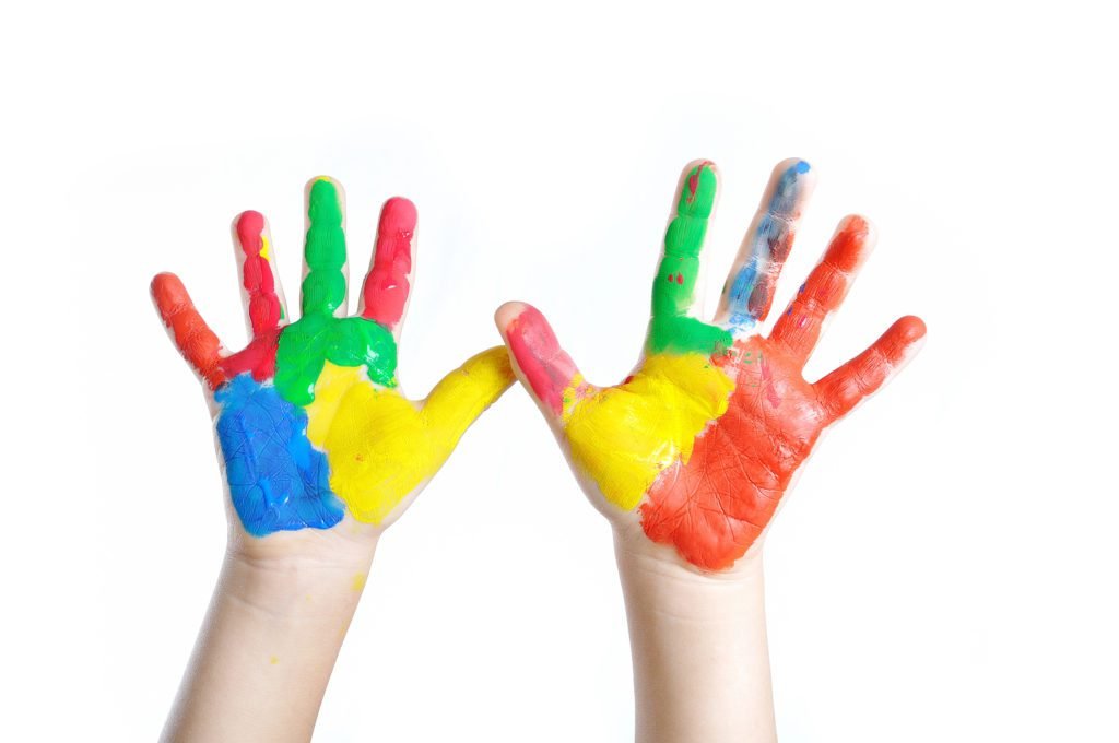 Descrição da imagem #pracegover: Foto de duas mãos de uma criança. Elas estão pintadas nas cores azul, amarelo, verde e vermelho, em menção ao símbolo do autismo. Fim da descrição.