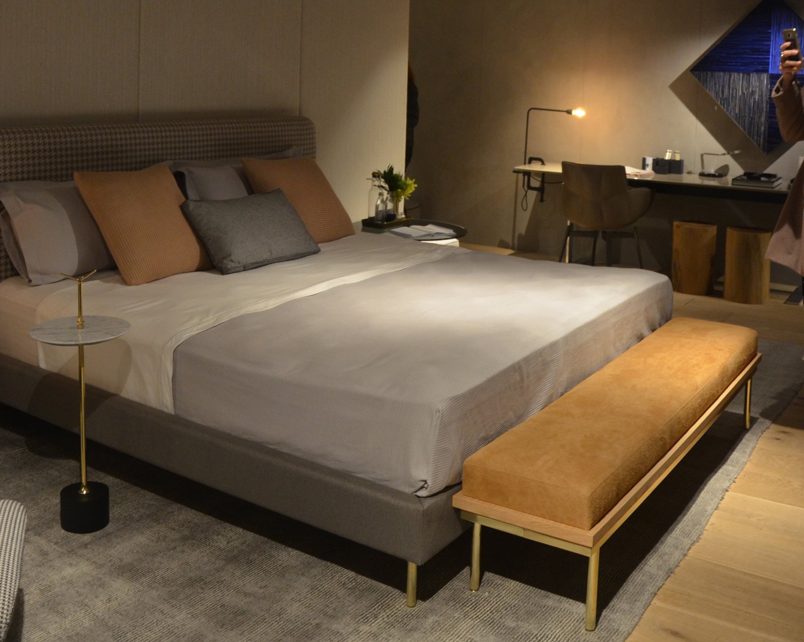 Descrição da imagem #PraCegoVer: Imagem no formato retangular, na horizontal. Um quarto muito aconchegante. Com uma cama em primeiro plano, um banco aos pés da cama, Ao fundo vemos uma escrivaninha. Em cima da cama, almofadas combinam com as cores da decoração do ambiente, em tons terrosos. Fim da descrição.