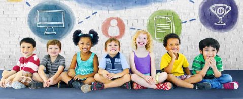 Descrição da imagem #PraCegoVer: Imagem no formato retangular, na horizontal. Um grupo de sete crianças estão sentadas no chão. As crianças são cinco meninos e duas meninas. Eles estão sorrindo e usam roupas coloridas. Fim da descrição.