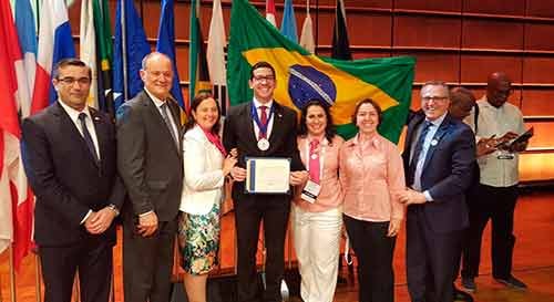 Descrição da imagem #PraCegoVer: Imagem no formato retangular, na horizontal. Parte da delegação brasileira que participou da conferência mundial do Woccu, realizada em Viena, na Áustria. Na imagem vemos quatro homens e três mulheres. Eles seguram a premiação recebida. Atrás deles, tem a bandeira do Brasil. Fim da descrição.