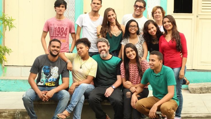 Descrição da imagem #PraCegoVer: Imagem no formato retangular, na horizontal. O cantor Wado com os participantes do clipe em Libras. São 13 pessoas. sendo seis homens e sete mulheres. Fim da descrição.