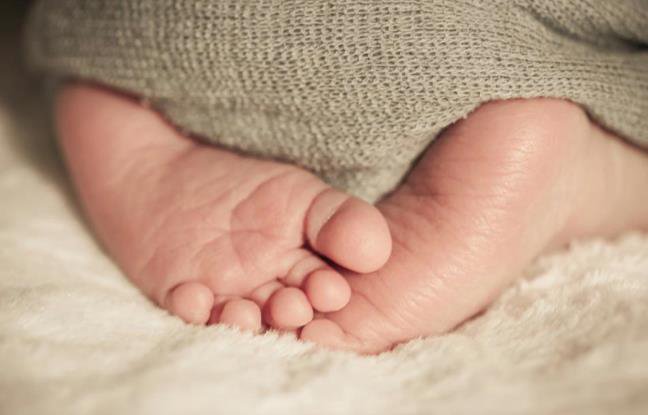 Descrição da imagem #pracegover: Dois pezinhos de um bebê, estão sobrepostos. O bebê está coberto por uma cobertinha cinza. Fim da descrição.