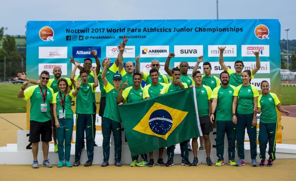 Descrição da imagem #PraCegoVer: Imagem no formato retangular, na horizontal. A delegação brasileira que participou do Mundial de Jovens de Atletismo. Eles estão usando uniforme verde e amarelo e seguram a bandeira do Brasil. Fim da descrição.
