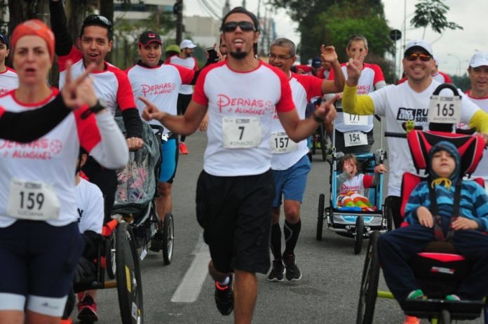 Descrição da imagem #PraCegoVer: Imagem no formato retangular, na horizontal. Um grupo de participantes do projeto Pernas de Aluguel durante uma corrida, que teve a participação de pessoas com deficiência. Entre os corredores, vemos três participantes em cadeiras de rodas. Fim da descrição.