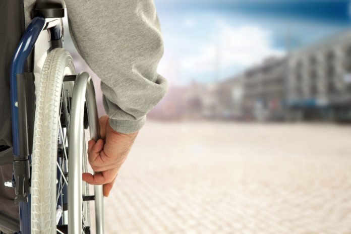 Descrição da imagem #PraCegoVer: Imagem no formato retangular, na horizontal. Uma pessoa em sua cadeira de rodas. É possível ver apenas uma lateral da cadeira, e a pessoa com a mão na roda. Á frente temos um caminho. Fim da descrição.
