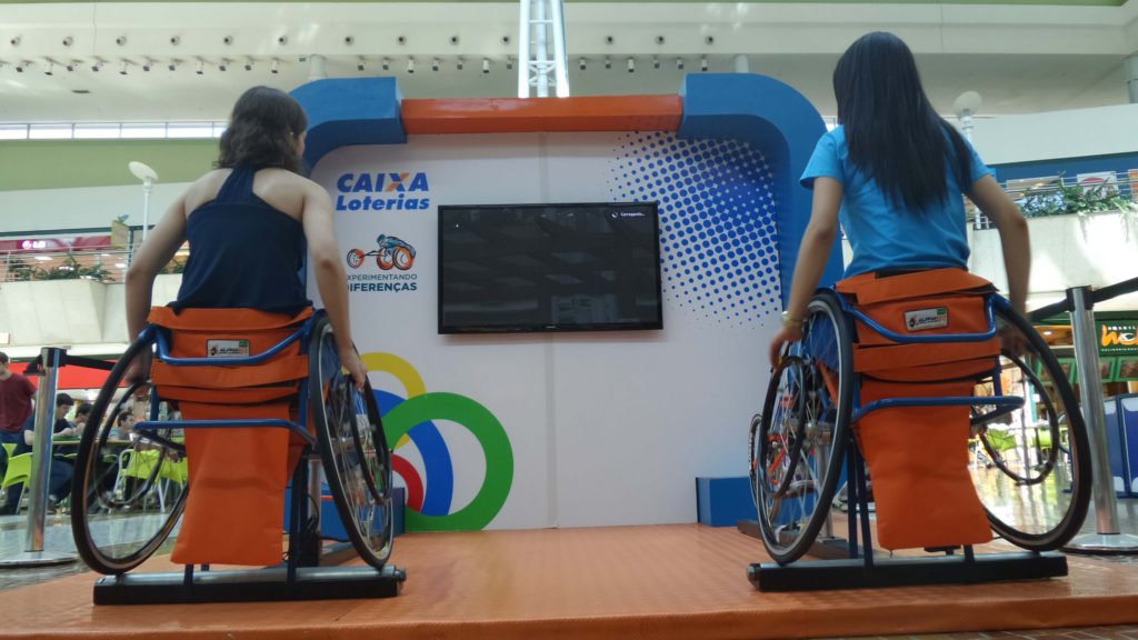 Descrição da imagem #PraCegoVer: Imagem no formato retangular, na horizontal. Duas meninas estão participando de uma atividade do Experimentando Diferenças. Elas estão sentadas em cadeiras de rodas. Fim da descrição.