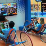 Descrição da imagem #PraCegoVer: Imagem no formato retangular, na horizontal. Duas pessoas estão participando de uma atividade do Experimentando Diferenças. Elas estão sentadas em handbikes. Fim da descrição.
