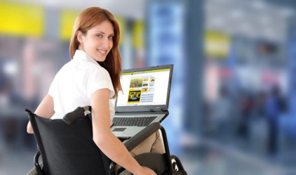 Descrição da imagem #PraCegoVer: Imagem no formato retangular, na horizontal. Uma moça está sentada em sua cadeira de rodas. Ela está com um notebook em seu colo, pesquisando informações sobre a linha de crédito para pessoas com deficiência. Ela está com o tronco levemente virado para trás e olha para a câmera. Fim da descrição.