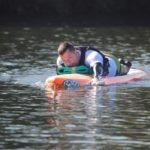 Descrição da imagem #PraCegoVer: Imagem no formato retangular, na horizontal. O atleta Alan Mazzoleni durante prática do paddleboard. Alan está deitado de bruços na prancha. Ele está no meio da represa. Fim da descrição.