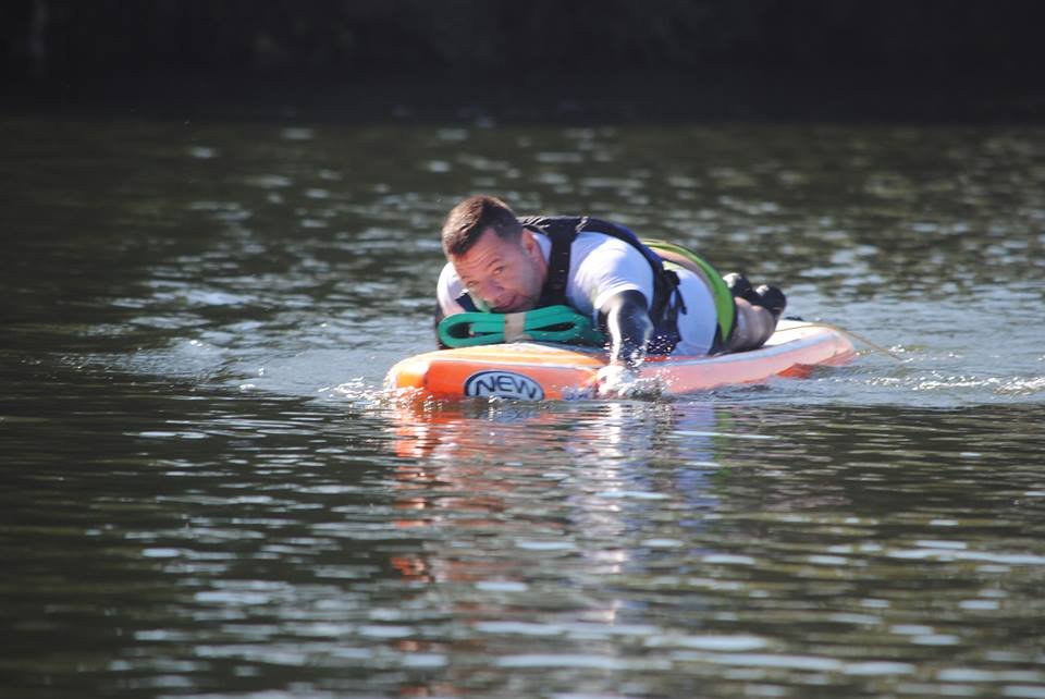 Descrição da imagem #PraCegoVer: Imagem no formato retangular, na horizontal. O atleta Alan Mazzoleni durante prática do paddleboard. Alan está deitado de bruços na prancha. Ele está no meio da represa. Fim da descrição.
