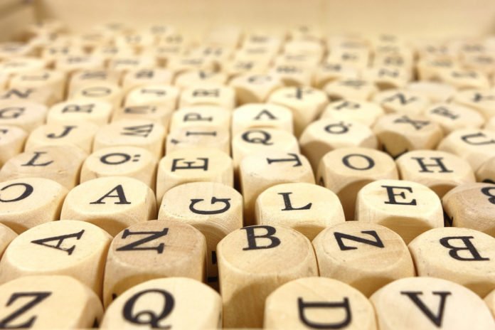 #descricaodaimagem #pracegover foto de vários cubos em madeira, com letras estampadas, estão sobre uma mesa. Fim da descrição.