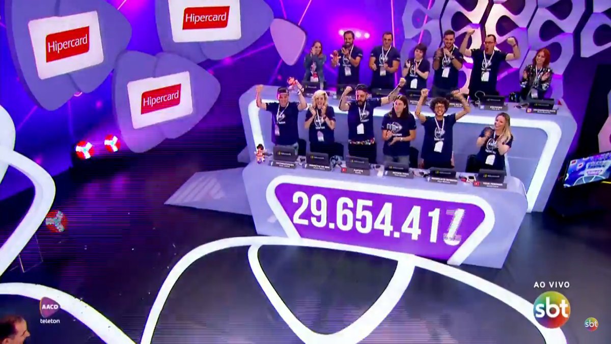 Descrição da imagem #PraCegoVer: Imagem no formato retangular, na horizontal. A bancada de influenciadores ao final do Teleton. Nela vemos os blogueiros que participaram da maratona e o painel com o valor total de doações, que superou a meta, chegando a 29 milhões 654 mil e 417 reais. Fim da descrição.