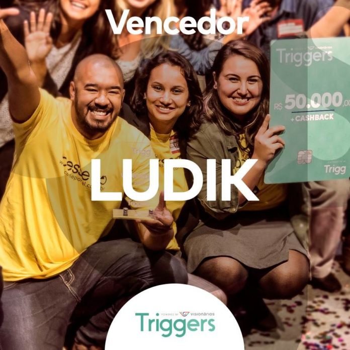 Descrição da Imagem #PraCegoVer: Foto no formato quadrado. Os três integrantes da equipe vencedora, após conquistar o prêmio. Eles estão usando uma camiseta amarela. Da esquerda para direita: Jansey Oliveira, Juliana Reis e Bianca Ponte, que está segurando o cartão de crédito da Trigg ilustrativo, em tamanho grande, com o valor de 50 mil reais. Fim da descrição.