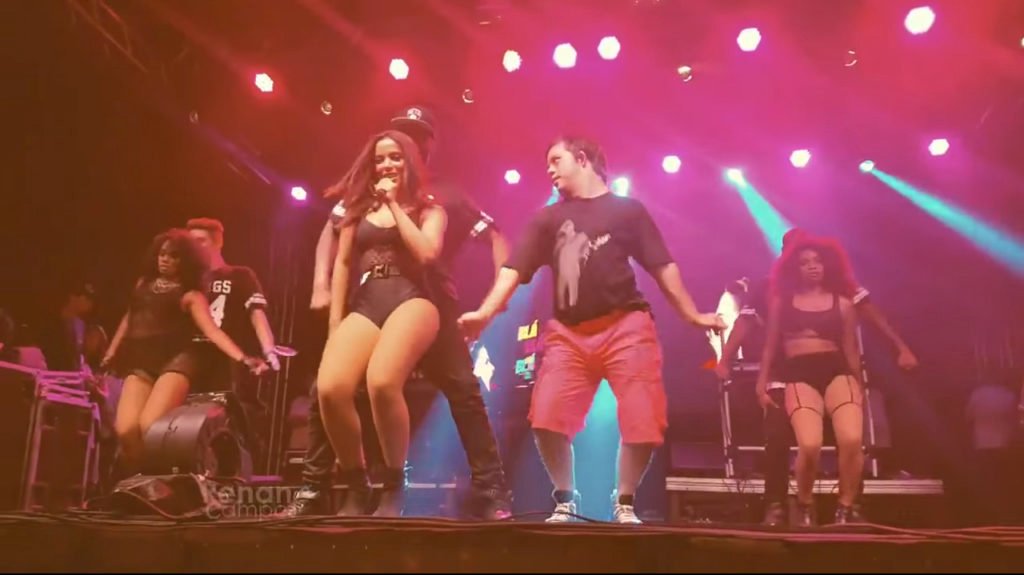 Descrição da imagem #PraCegoVer: Imagem no formato retangular, na horizontal. A cantora Anitta durante um de seus shows. Ela está no palco, ao lado de seu novo bailarino que tem síndrome de Down. Fim da descrição.