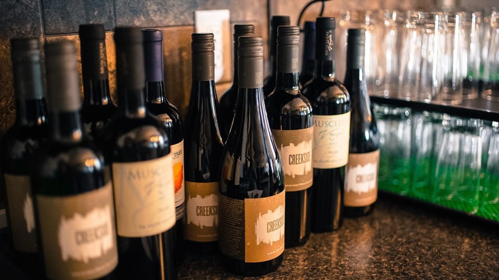 Descrição da imagem #PraCegoVer: Imagem no formato retangular, na horizontal. Várias garrafas de vinho estão sobre uma bancada de madeira. Fim da descrição.