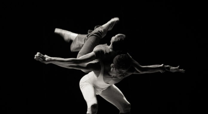 Descrição da imagem #PraCegoVer: Imagem no formato retangular, na horizontal. A foto, em preto e branco. Nela, dois bailarinos da cia. de ballet de cegos, um homem e uma mulher, fazem uma coreografia. Fim da descrição.