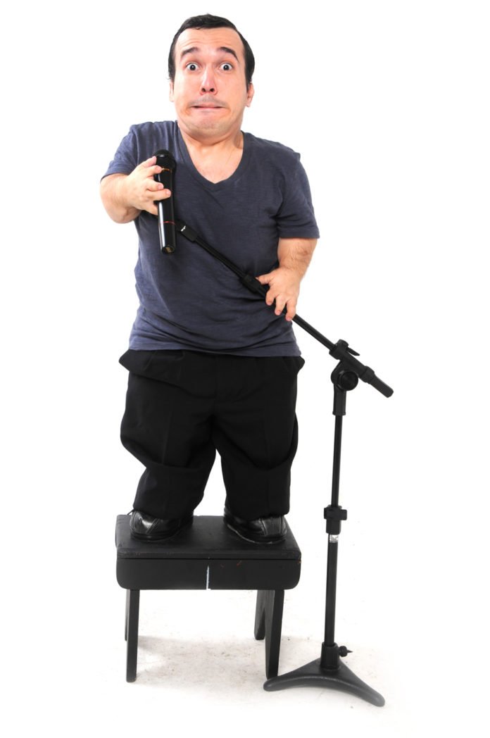 Descrição da Imagem #pracegover: Foto do Gigante Leo durante uma de suas apresentações de stand up comedy. Leo está em cima de um banquinho preto e tem um microfone à sua frente. Fim da descrição.