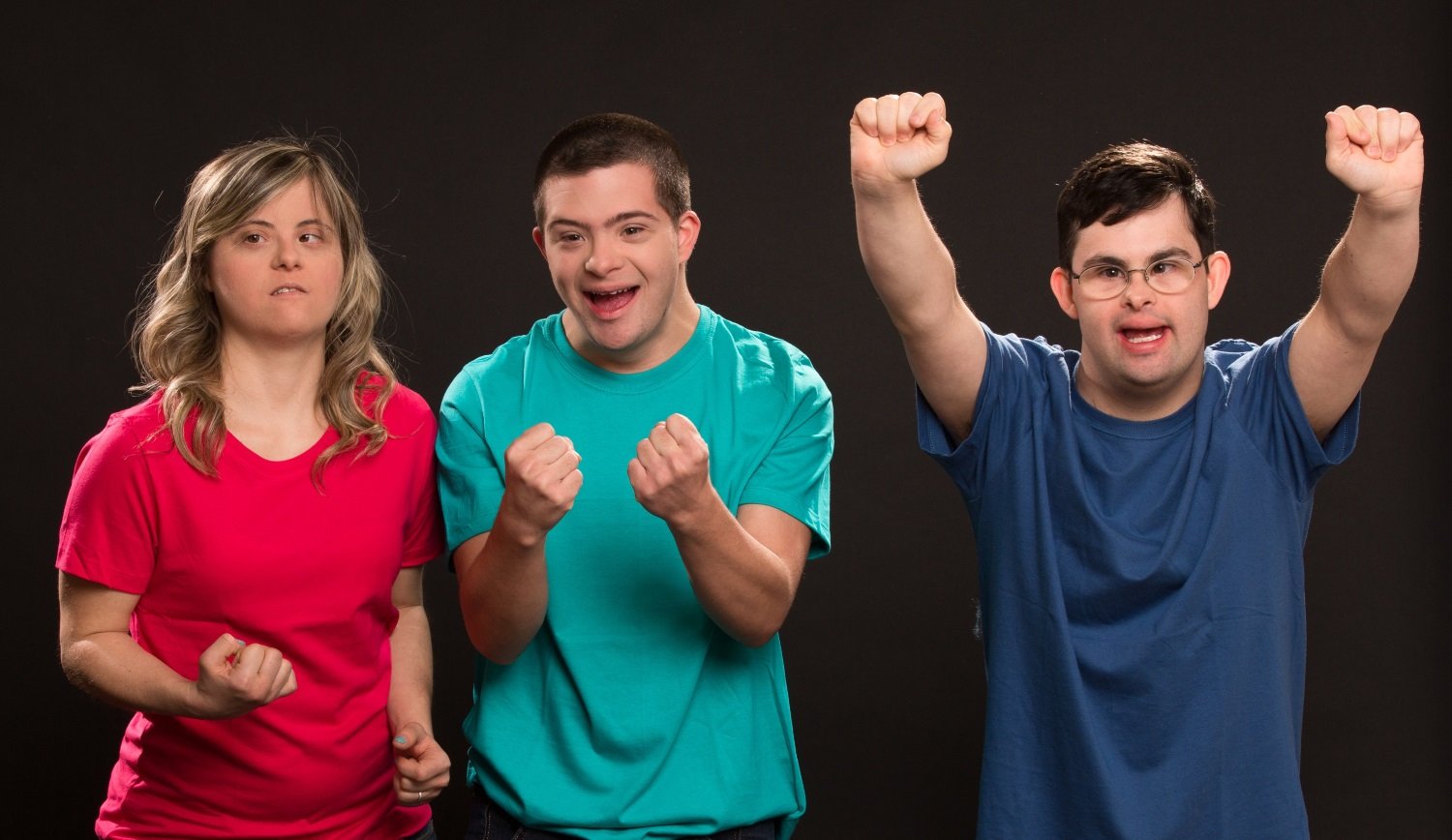 Descrição da imagem #PraCegoVer: Imagem no formato retangular, na horizontal. Os atores João Simões Junior, Ian Pereira e Giulia Merigo, que têm síndrome de Down, durante cena da montagem Colegas no Teatro. Eles usam camisetas coloridas. Fim da descrição.