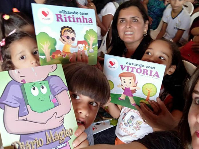 Descrição da imagem #PraCegoVer: Imagem no formato retangular, na horizontal. A escritora Sharlene Serra com alunos de uma escola. As crianças estão segurando os livros da Coleção Incluir. Fim da descrição.