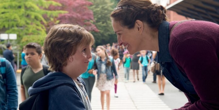 Descrição da imagem #PraCegoVer: Imagem no formato retangular, na horizontal. Cena do filme Extraordinário. Nela Julia Roberts conversa com o menino, protagonista da história, na porta da escola. Eles estão de perfil, e ao fundo vemos uma movimentação de pessoas. O menino tem uma malformação facial. Fim da descrição.