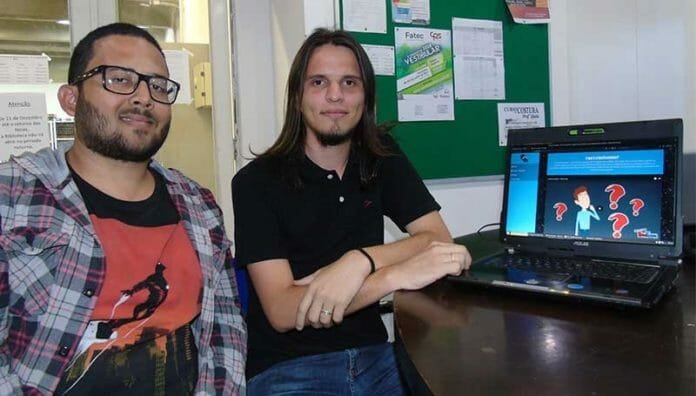 Descrição da imagem #PraTodosVerem: Imagem no formato retangular, na horizontal. Os universitários Matheus e Tiago. Eles estão ao lado de um computador, com a tela do programa premiado. Fim da descrição.