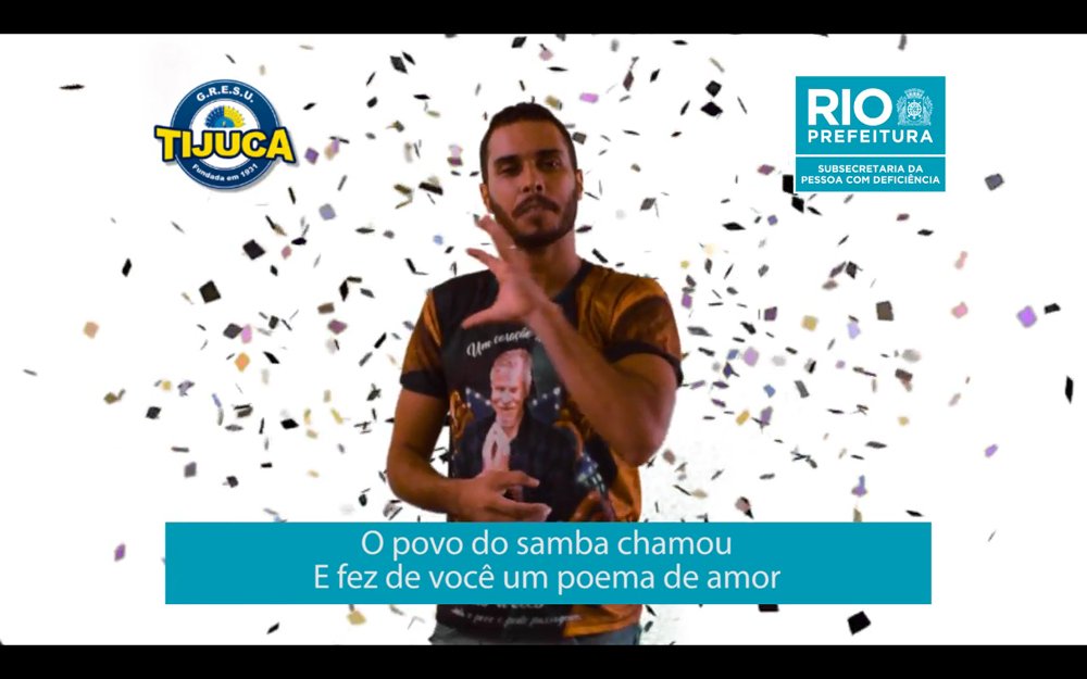 Descrição da imagem #PraTodosVerem: Imagem no formato retangular, na horizontal. Imagem do clipe em Libras da escola de samba Unidos da Tijuca. O intérprete está usando a camisa da escola de samba, que tem a imagem de Miguel Fallabela, homenageado. Fim da descrição.