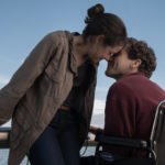 Descrição da imagem #PraCegoVer: Imagem no formato retangular, na horizontal. Cena do filme O que te faz mais forte. Os protagonistas estão se beijando. A mulher está de pé e o rapaz está sentado em sua cadeira de rodas. Fim da descrição.