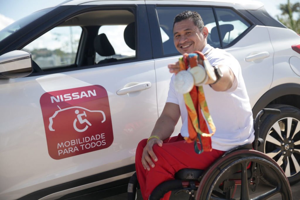 Descrição da imagem #PraCegoVer: Imagem no formato retangular, na horizontal. O paratleta Clodoaldo Silva, posa com suas medalhas. Ele está ao lado de um Nissan Kicks branco. Na porta do carro está um adesivo escrito "Nissan Mobilidade Para Todos". Fim da descrição.