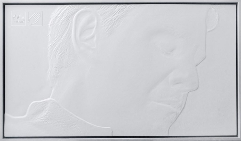 Descrição da imagem #PraCegoVer: Imagem no formato retangular, na horizontal. Obra que compõe a exposição tátil. Um quadro todo branco, com a imagem do rosto de um homem, de perfil. A imagem está em alto relevo. Fim da descrição.
