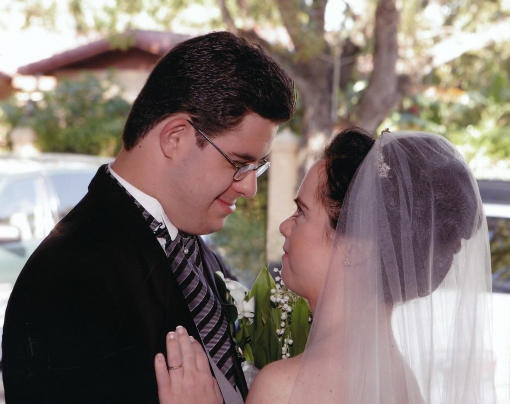 Descrição da imagem #PraCegoVer: Imagem no formato retangular, na horizontal. Cena do filme Monica & David. Um rapaz e uma moça, com síndrome de Down, em seu casamento. Ele está de terno preto e ela de vestido de noiva branco. Fim da descrição.