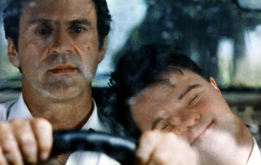 Descrição da imagem #PraCegoVer: Imagem no formato retangular, na horizontal. Cena do filme O oitavo dia. Um homem e um rapaz com síndrome, no carro. O homem está dirigindo e o rapaz está com a cabeça em seu ombro. Fim da descrição.