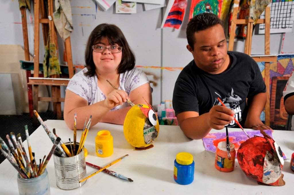 Descrição da imagem #PraCegoVer: Imagem no formato retangular, na horizontal. Dois jovens com deficiência intelectual em atividade na sede da APAE DE SÃO PAULO. Eles estão realizando uma atividade de artes. Fim da descrição.