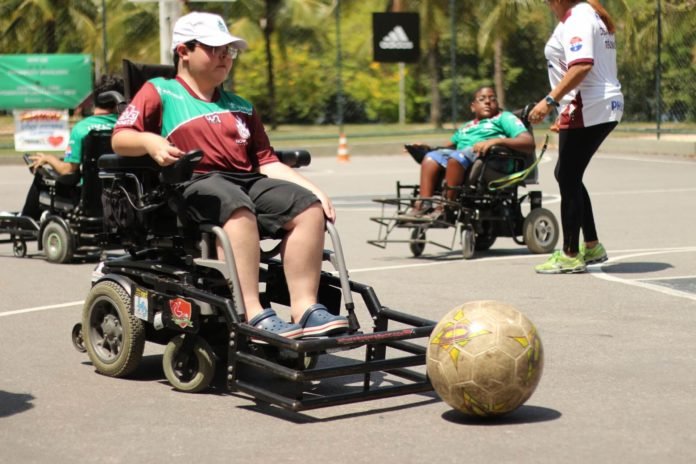 Descrição da imagem #PraCegoVer: Imagem no formato retangular, na horizontal. Treino de Power Soccer. Vemos dois homens nas cadeiras de rodas adaptadas para a modalidade. eles estão em uma quadra. Fim da descrição.