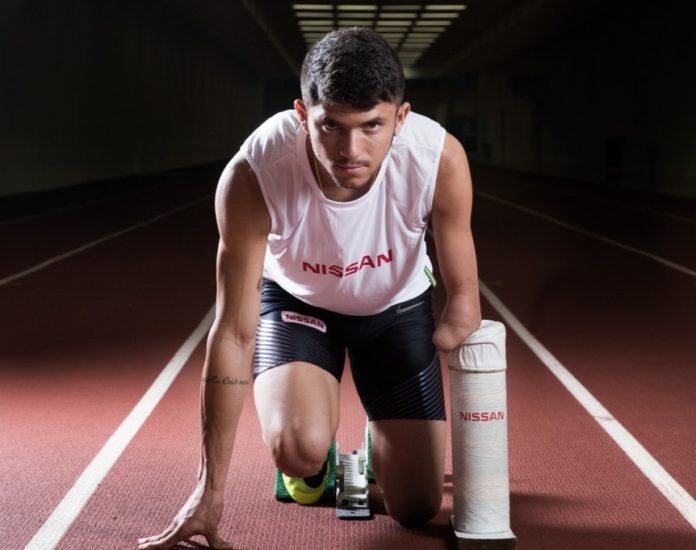 Descrição da imagem #PraCegoVer: Imagem no formato retangular, na horizontal. O atleta Petrúcio Ferreira, em posição de largada, em uma pista de atletismo. Petrúcio é um rapaz moreno, com cabelos castanhos escuros. Ele tem uma amputação de membro superior esquerdo. Fim da descrição.