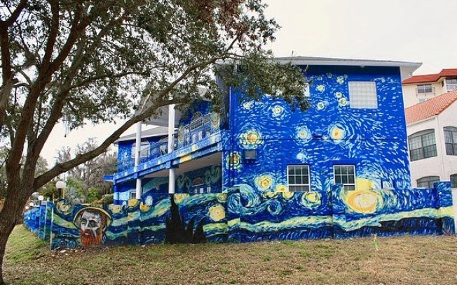 Descrição da imagem #PraCegoVer: Imagem no formato retangular, na horizontal. A fachada da casa Van Gogh. A casa é pintada na cor azul, com detalhes nas cores amarelo e branco. Trata-se de uma reprodução da obra 'A noite estrelada' de Van Gogh. Fim da descrição.